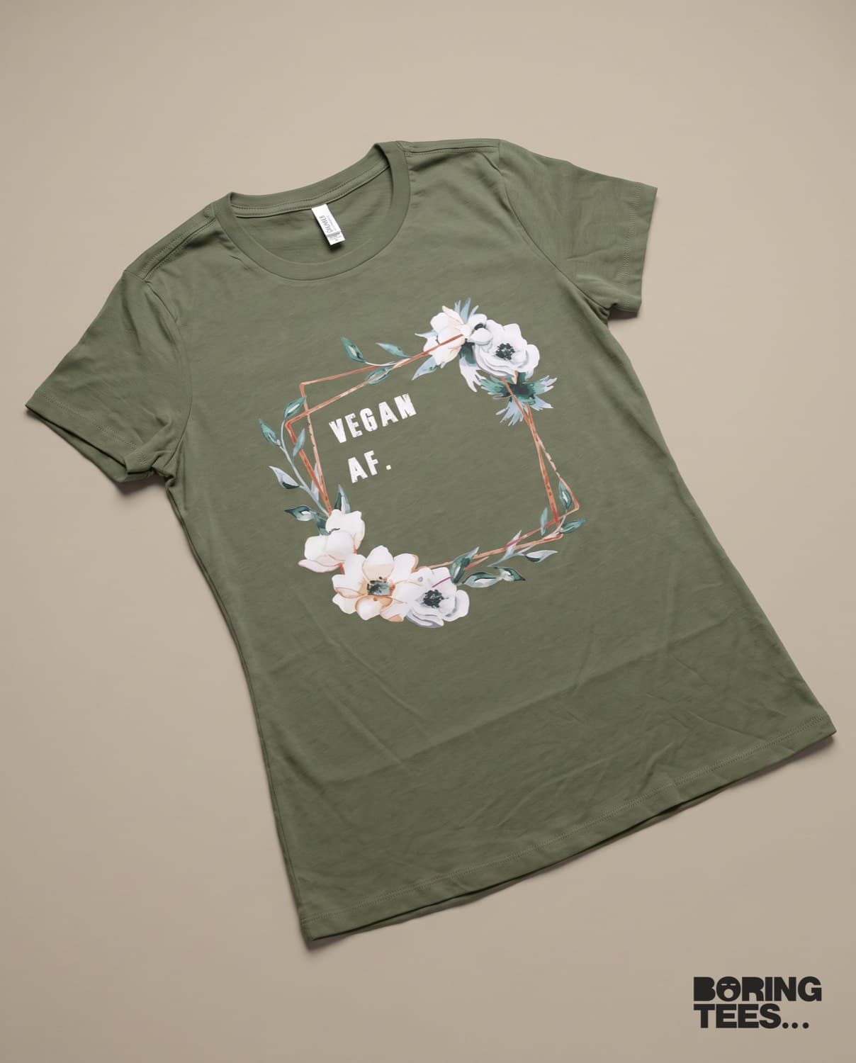 Olive green tee with a watercolour floral wreath and copper geometric frame around the words VEGAN AF